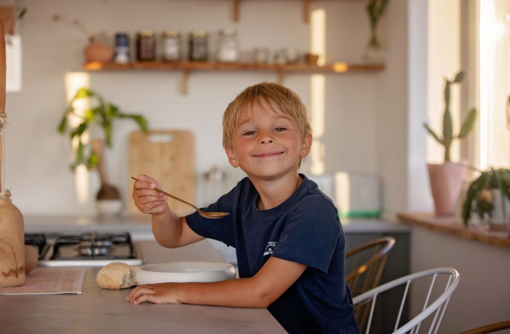 An older child smiles as they enjoy a bowl of warm soup following their tooth extraction.