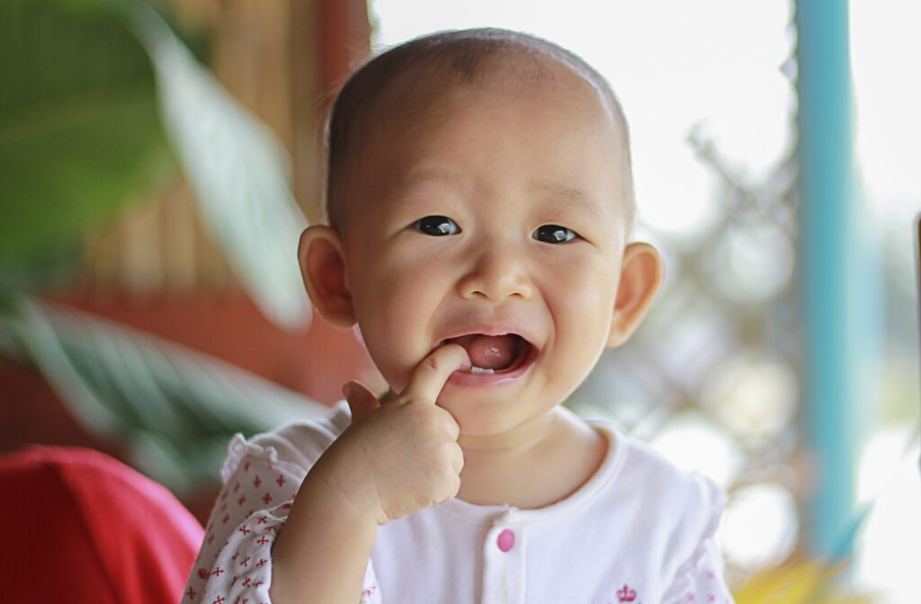 A young baby sticking their index finger in their mouth to rub their teeth due to discomfort.